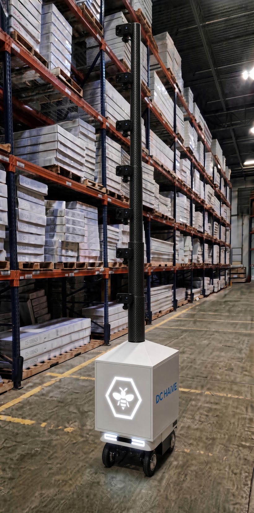 The DC HAiVE rover parked in a distribution center aisle beside loaded pallet racking. A rigid carbon-fiber mast rises from the vehicle body carrying seven camera positions, each aimed at the rack face.